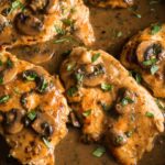 Top-down view of a classic Chicken Marsala in a cast iron skillet, with golden-brown chicken pieces simmered in a rich, dark gravy, garnished with mushrooms and fresh parsley.