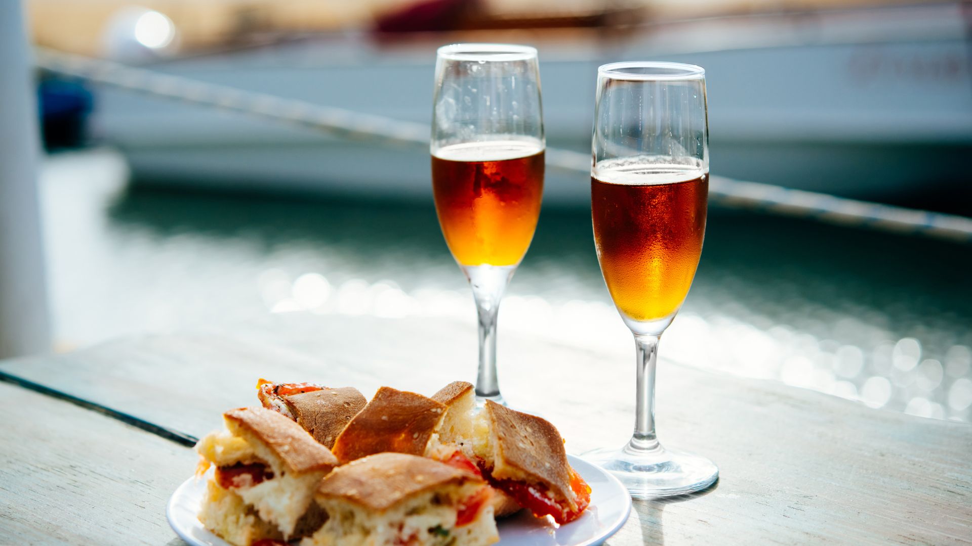 Two glasses of Marsala wine next to a plate of finger sandwiches. Sunlight highlights the rich amber color of this famous Sicilian fortified wine.