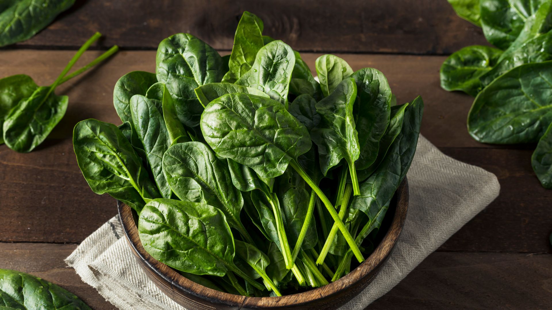 A bunch of fresh spinach leaves on a wooden surface, their deep green color and crinkled texture catching the light.