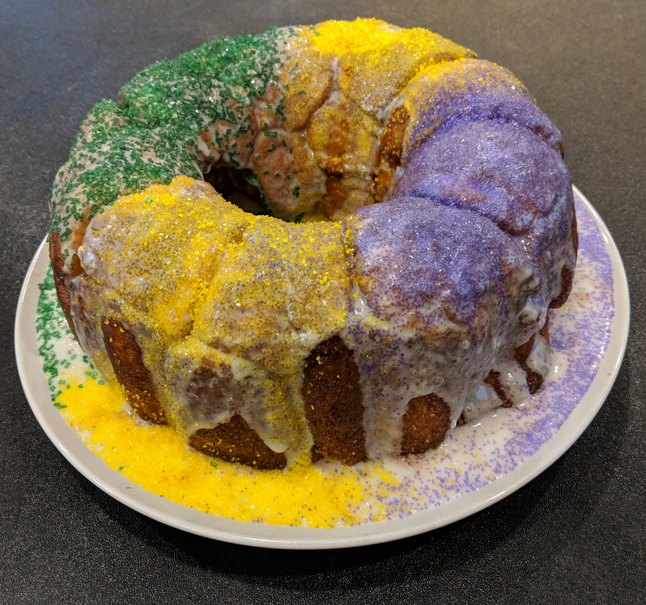 Mardi Gras King Cake decorated with green, purple, and gold sprinkles over white glaze.