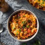Bowl of Chili Mac with melted cheese and fresh parsley, with pasta, beans, and tomatoes in a rich sauce.